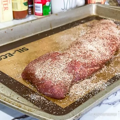 Raw pork tenderloin covered in seasoning on a baking sheet