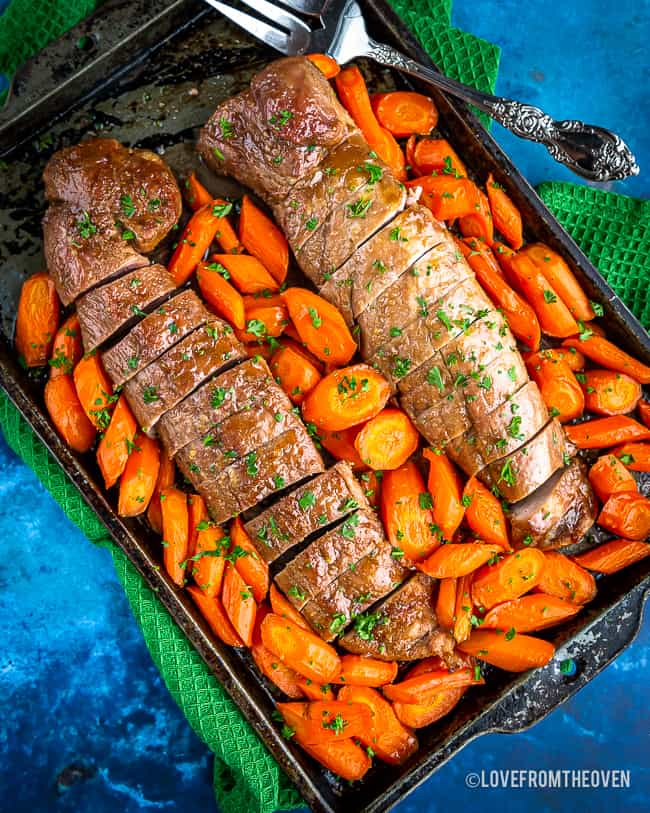 Pork tenderloin on a tray surrounded by seasoned carrots