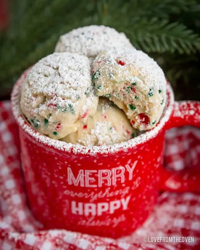 Red mug full of snowball cookies topped with powdered sugar