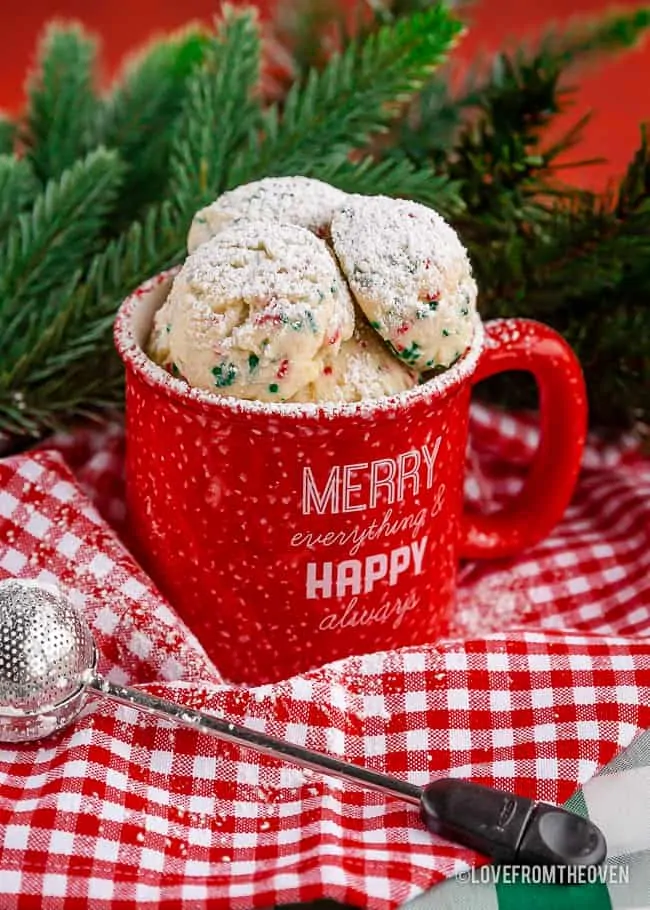 Several snowball cookies in a red mug on a red and white napkin