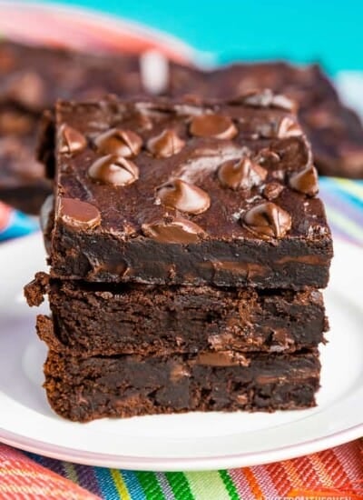 A stack of three black bean brownies, on a white plate with a colorful napkin and a blue background