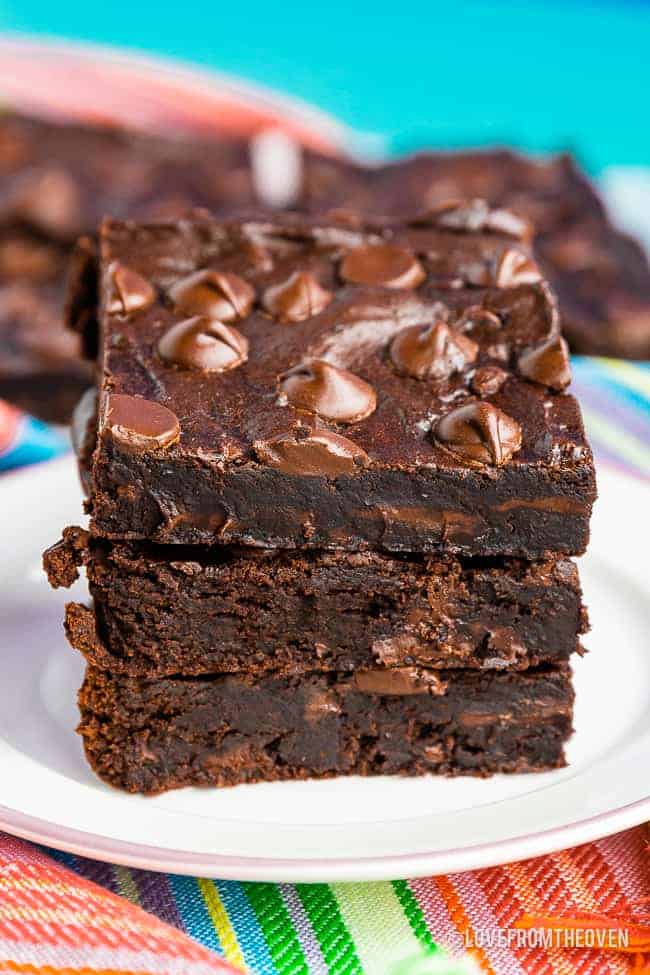 A stack of three black bean brownies, on a white plate with a colorful napkin and a blue background