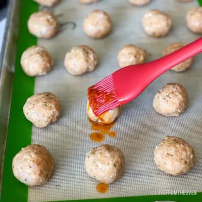 Chicken parm meatballs on baking sheet being brushed with sauce