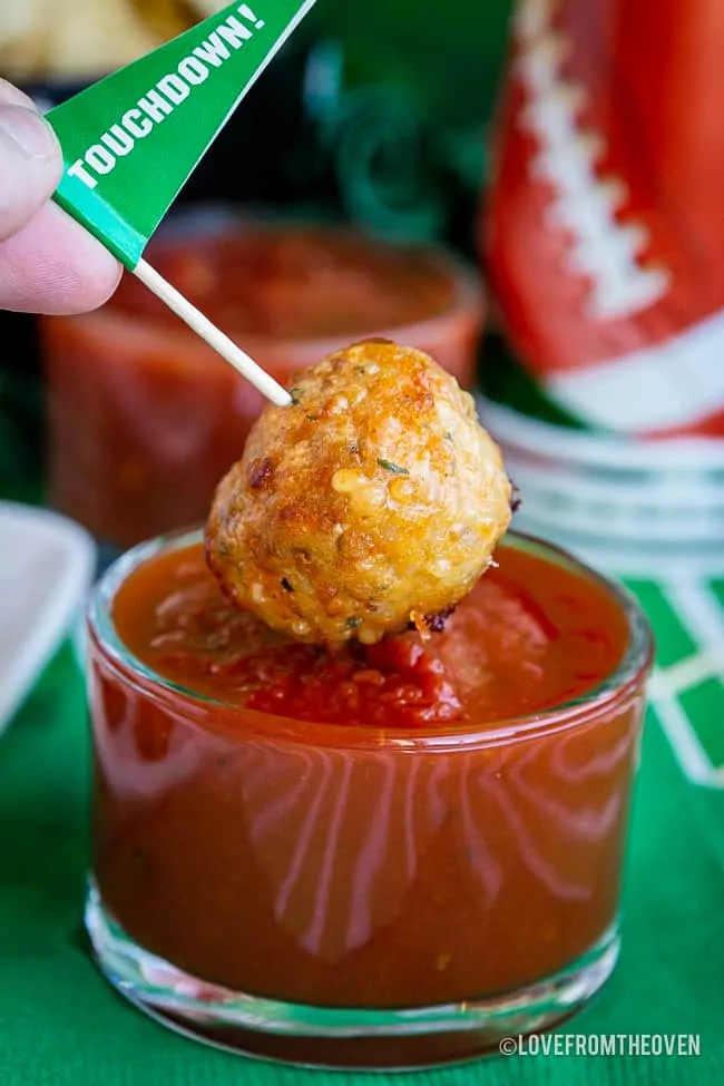 Chicken parm meatballs being dipped into marinara sauce
