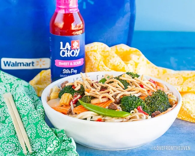 Bowl of chow mein in front of a bottle of sweet and sour sauce