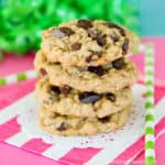 A stack of oatmeal chocolate chip cookies with a pink and white napkin and a blue and green background