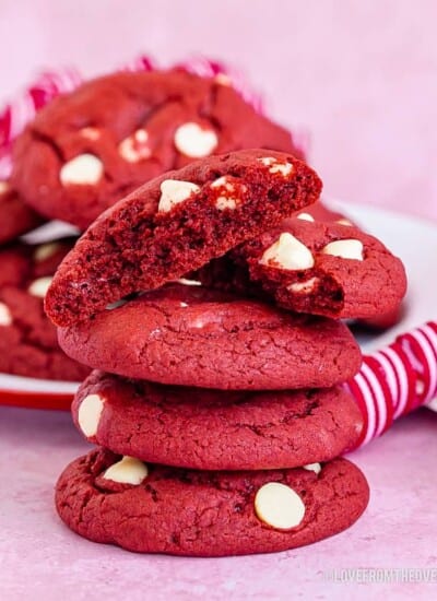 A stack of red velvet cake mix cookies with white chocolate chips on a pink background