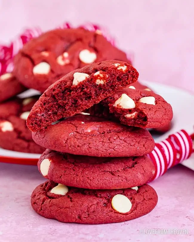 A stack of red velvet cake mix cookies with white chocolate chips on a pink background