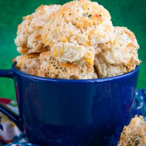 A blue bowl full of cheddar bay biscuits in front of a green backgroud