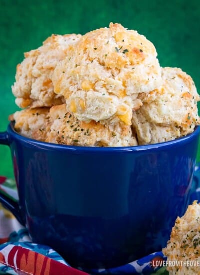 A blue bowl full of cheddar bay biscuits in front of a green backgroud