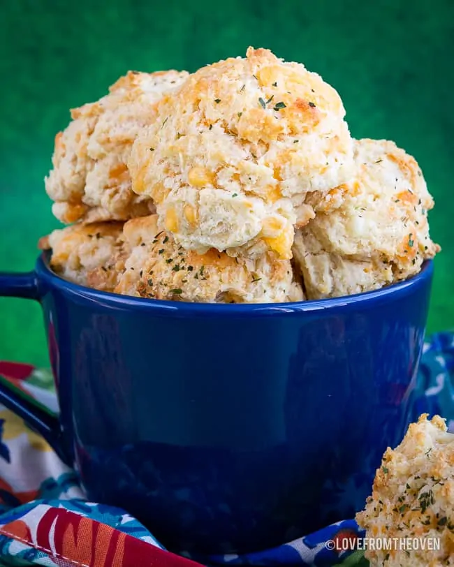 A blue bowl full of cheddar bay biscuits in front of a green backgroud