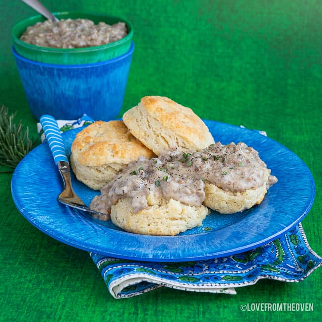 A blue cup sitting on top of a plate of food, with Gravy and Biscuit