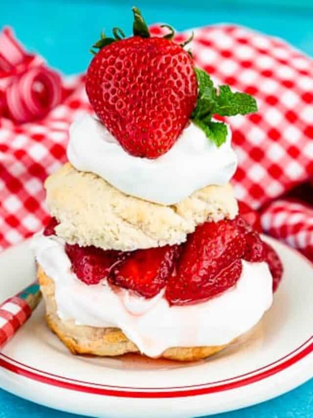 A serving of strawberry shortcake on a white plate with a blue background