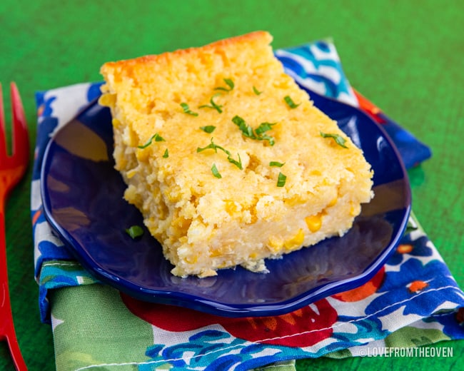 A slice of corn pudding casserole on a blue plate and floral napkin