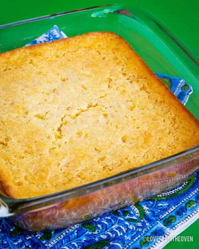 A square pan of corn pudding casserole on a green backround