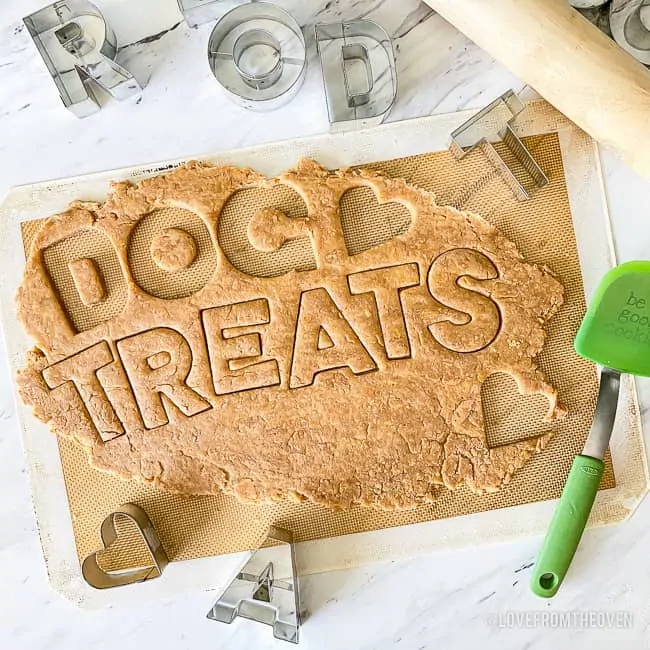 Dough for peanut butter dog treats, rolled out, with cookie cutters cutting out the words dog treats