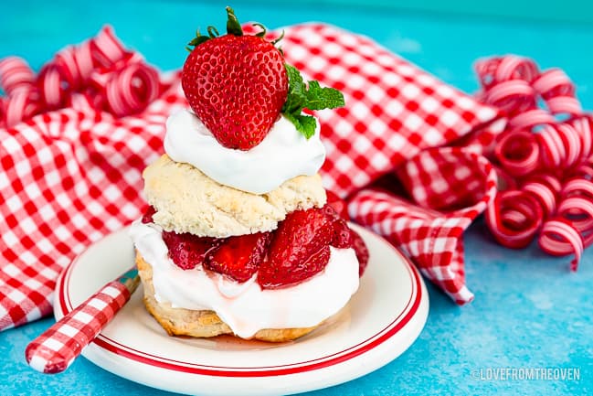A serving of strawberry shortcake on a white plate with a blue background
