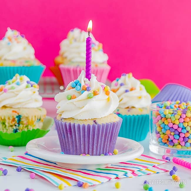 Funfetti cupcakes on a table, one with a lit candle in it