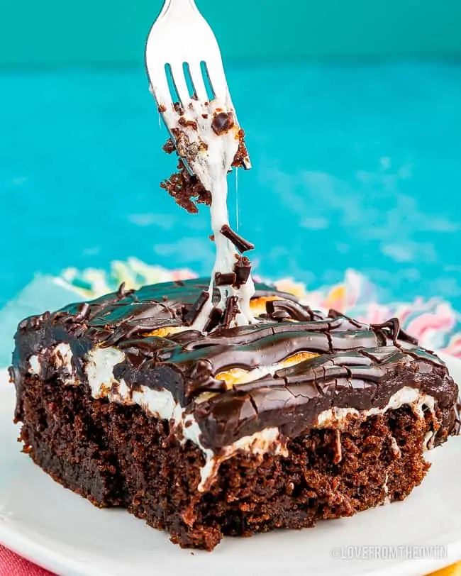 A slice of chocolate sheet cake with marshmallows and frosting and a fork grabbing a piece