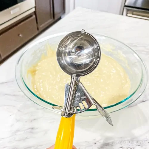 An ice cream scoop in front of a bowl of pancake batter