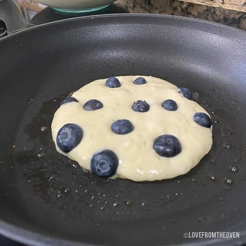 Blueberry pancake being cooked in a skillet