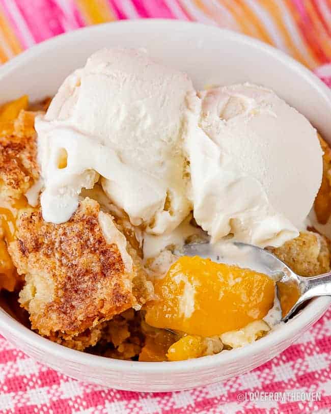 Bowl of peach dump cake topped with vanilla ice cream