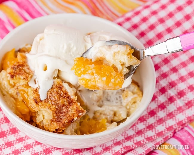 Bowl of peach dump cake with vanilla ice cream melting on top