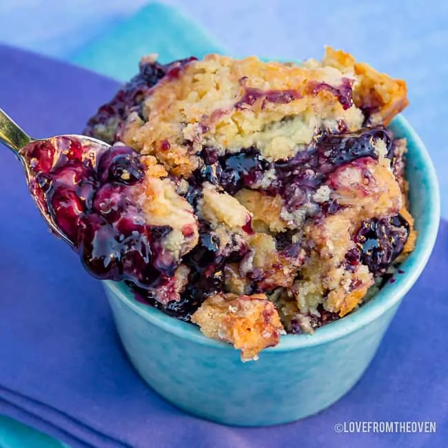 Cup of blueberry dump cake with a spoon taking out a bite