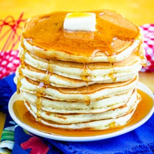 A stack of buttermilk pancakes topped with syrup and butter