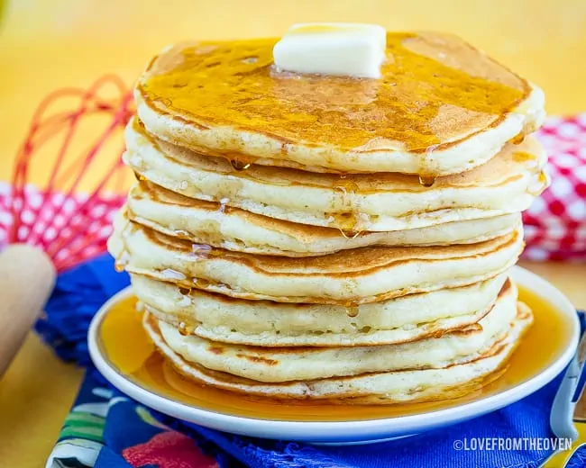 A stack of pancakes, topped with syrup and butter