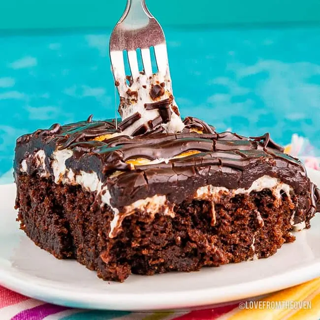 A slice of chocolate cake topped with chocolate frosting and marshmallow topping