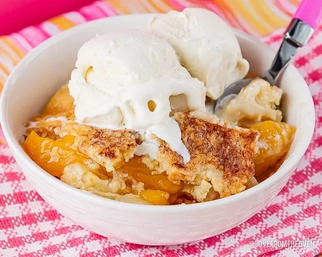 White bowl with peach dump cake and ice cream in it
