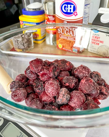A bowl of frozen cherries with ingredients behind it