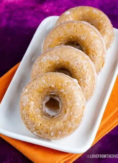 Four glazed pumpkin donuts on a tray