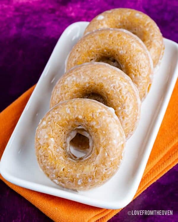 Four glazed pumpkin donuts on a tray