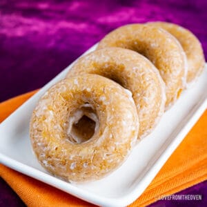 Four pumpkin donuts laying on a white tray