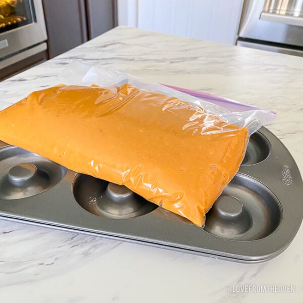 batter for pumpkin donuts in a ziploc bag on top of a donut pan