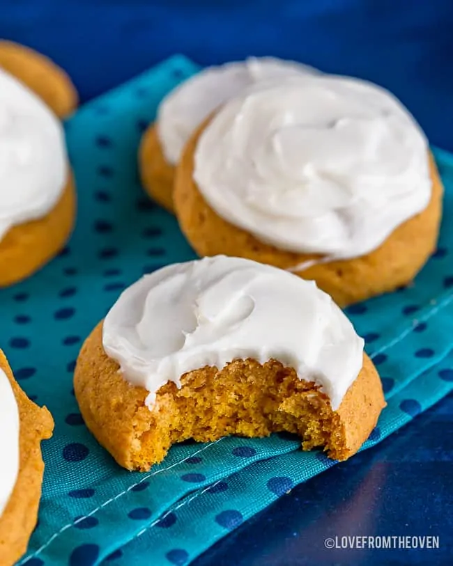 frosted pumpkin cookies, one with a bite taken out, on a blue background