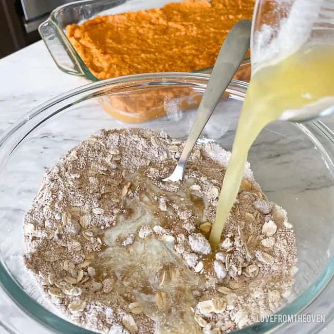 Butter being poured into a crumb topping mixture in a bowl