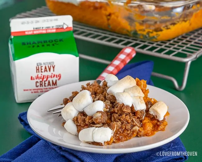 Sweet Potato Marshmallow Casserole on a plate with a carton of whipping cream next to it