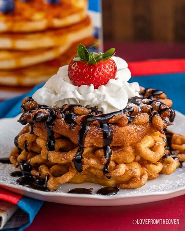 A stack of funnel cakes with chocolate sauce and whipped cream on top