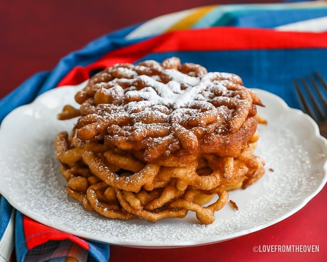 funnel-shaped cake covered with powdered sugar on a white plate