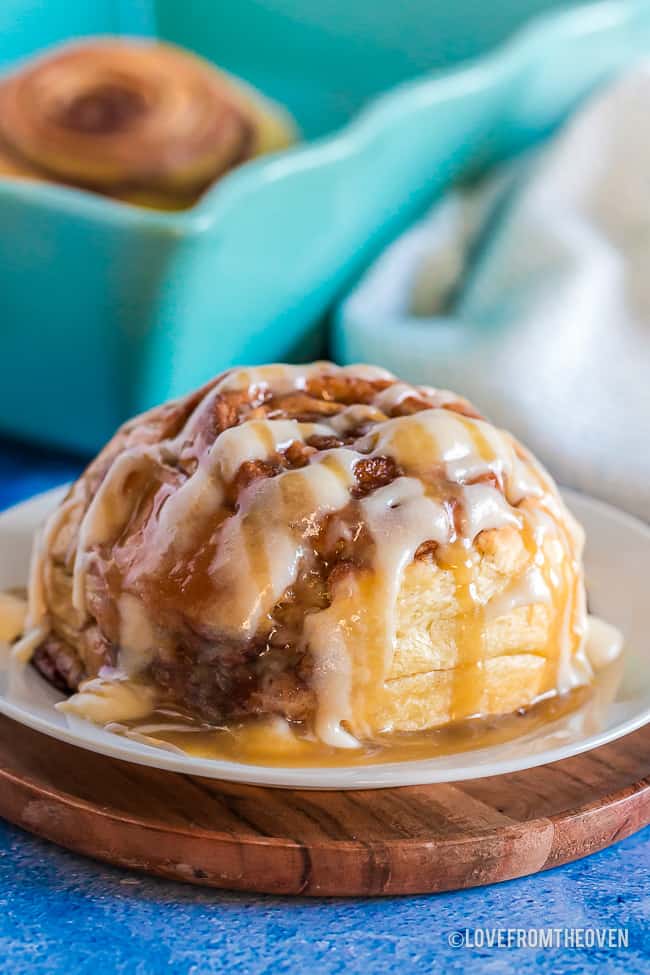 A homemade cinnamon roll on a white plate with a blue background