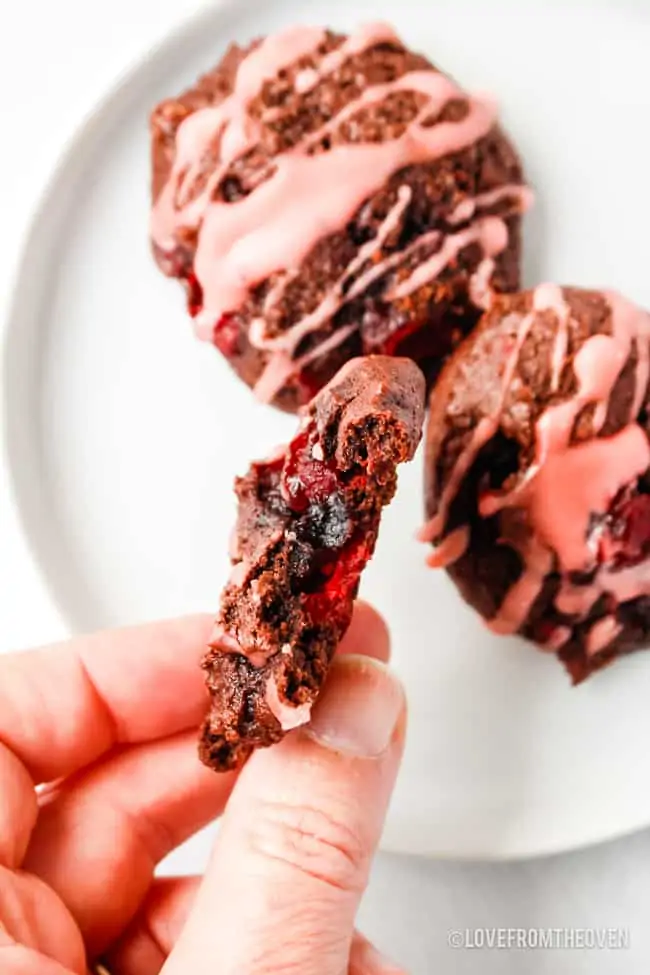 a hand holding a cherry chocolate cookie with a bite out of it