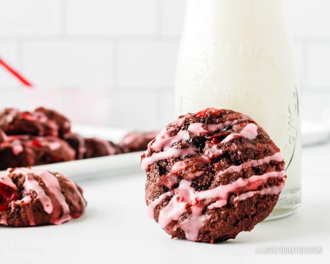 A chocolate cake mix cookie with cherries leaning against a glass of milk