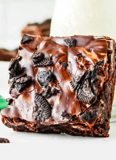 A mint oreo brownie sitting against a glass of milk