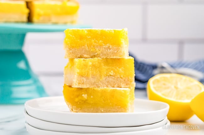 A stack of lemon bars on a white plate with a lemon behind it.
