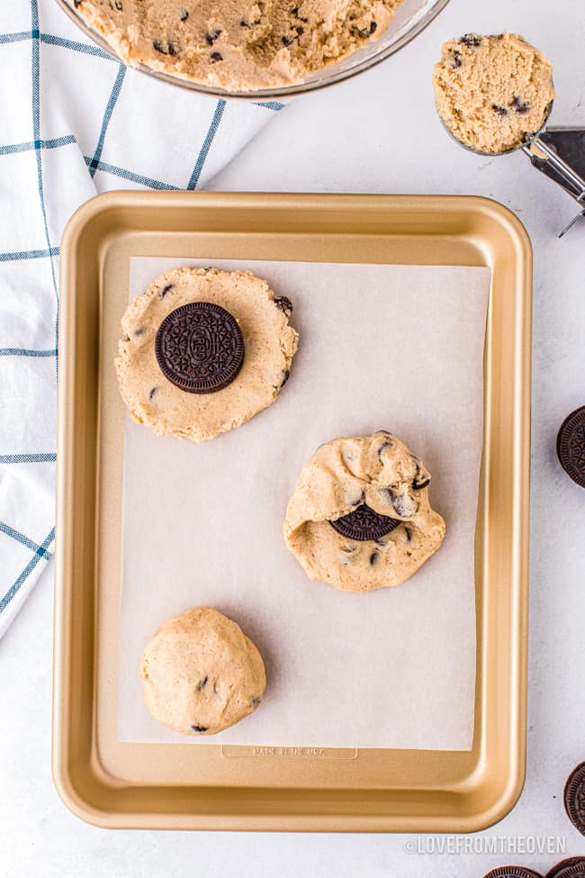 A tray of chocolate chip cookie dough with oreos being placed inside