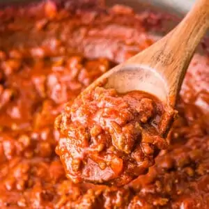 A pan of homemade spaghetti sauce with a spoon stirring