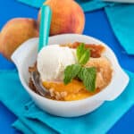 a bowl of peach cobbler made with canned peaches on a blue background